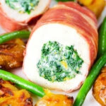 Close-up chicken wrapped in Parma ham stuffed with spinach and ricotta served with roasted new potatoes and green beans.