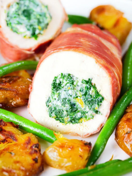 Close-up chicken wrapped in Parma ham stuffed with spinach and ricotta served with roasted new potatoes and green beans.