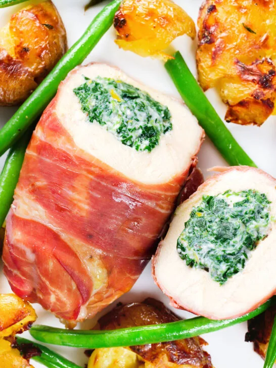 Close-up overhead chicken wrapped in Parma ham stuffed with spinach and ricotta served with roasted new potatoes and green beans.