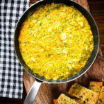 Overhead canned crab and saffron risotto served in a pan with dill and garlic bread.