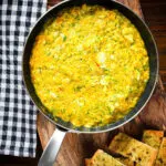Overhead canned crab and saffron risotto served in a pan with dill and garlic bread.