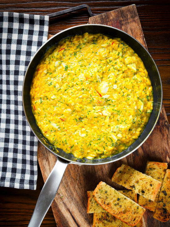 Overhead canned crab and saffron risotto served in a pan with dill and garlic bread.