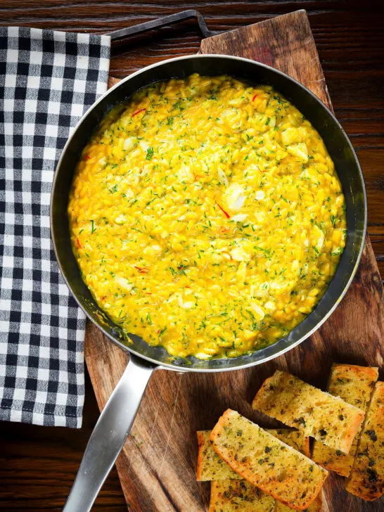 Overhead canned crab and saffron risotto served in a pan with dill and garlic bread.
