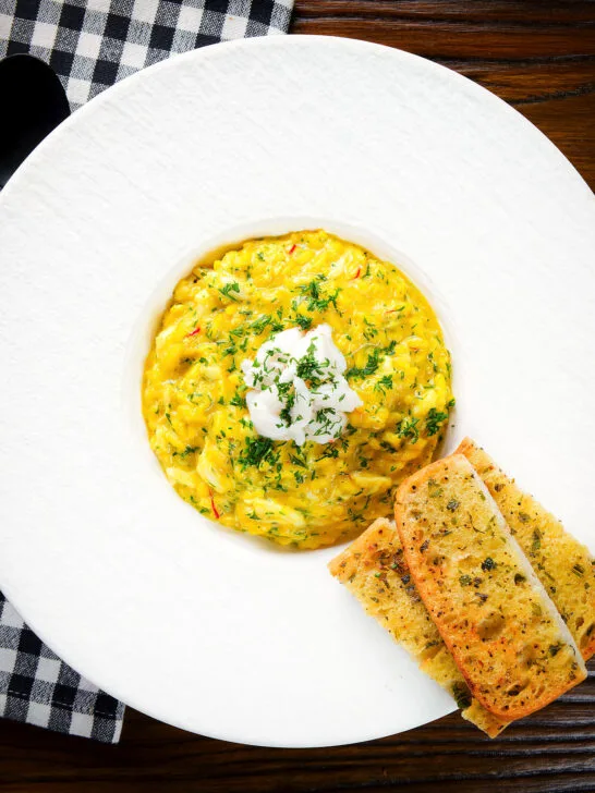 Overhead canned crab and saffron risotto served with dill and garlic bread.