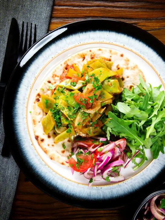 Overhead taze fasulye (Turkish green bean stew) served on flatbread with piyaz salad.