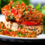 Close-up tinned sardines on toast in tomato sauce with capers, fresh tomato, and chilli.