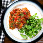 Overhead tinned sardines on toast in tomato sauce with capers, fresh tomato, and chilli.