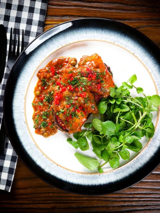 Overhead tinned sardines on toast in tomato sauce with capers, fresh tomato, and chilli.