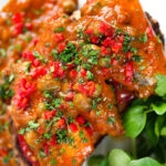 Close-up overhead tinned sardines on toast in tomato sauce with capers, fresh tomato, and chilli.