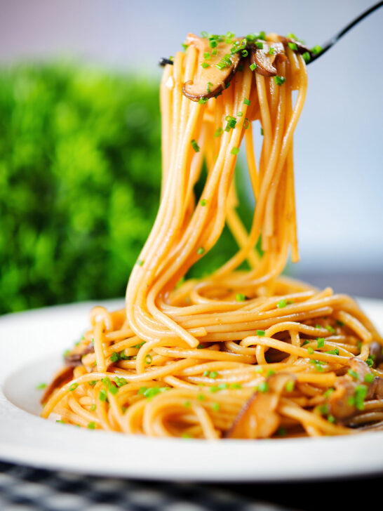 Vegetarian miso mushroom pasta (spaghetti) with snipped chives being picked up with a fork.