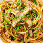 Close-up overhead vegetarian miso mushroom pasta (spaghetti) with snipped chives.