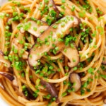 Close-up overhead vegetarian miso mushroom pasta (spaghetti) with snipped chives.