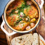 Coq au vin blanc or chicken in a white wine sauce served in a pot with French baguette.