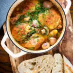 Coq au vin blanc or chicken in a white wine sauce served in a pot with French baguette.