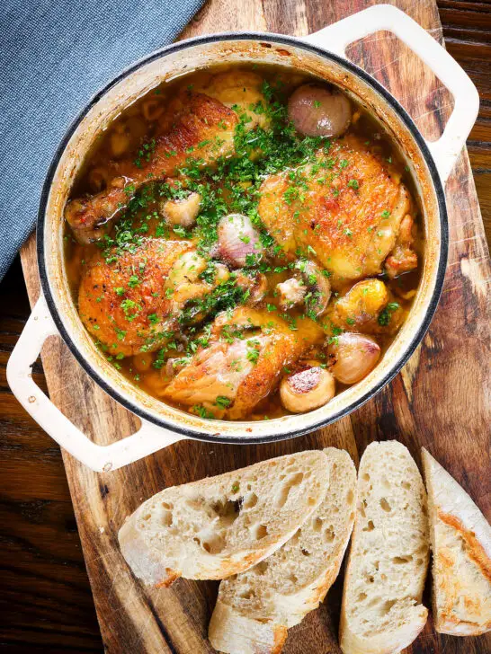 Coq au vin blanc or chicken in a white wine sauce served in a pot with French baguette.