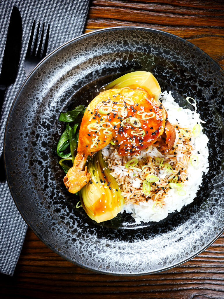 Overhead Chinese influenced soy sauce braised chicken leg with pak choi and rice.