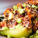 Close-up spicy sticky sesame tofu served with pak choi and jasmine rice.