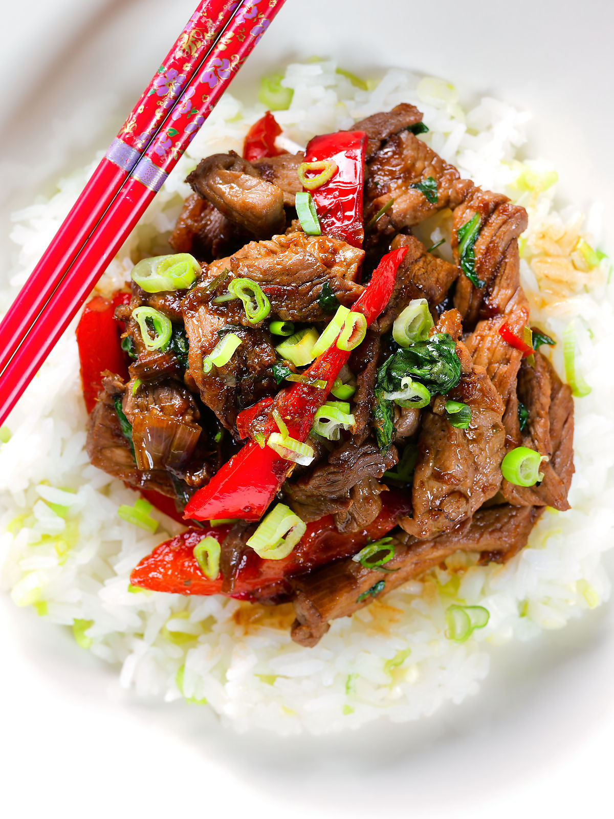 Close-up overhead spicy Thai basil and beef stir fry served with jasmine rice and spring onions.