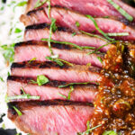 Close-up Thai Crying Tiger Steak with a spicy dipping sauce, rice, and tomato and cucumber salad.