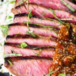Close-up Thai Crying Tiger Steak with a spicy dipping sauce, rice, and tomato and cucumber salad.
