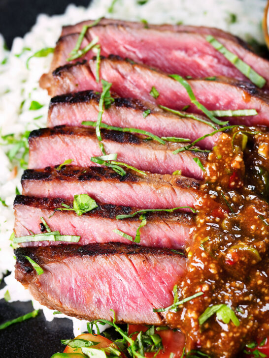 Close-up Thai Crying Tiger Steak with a spicy dipping sauce, rice, and tomato and cucumber salad.