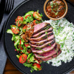 Overhead Thai Crying Tiger Steak with a spicy dipping sauce, rice, and tomato and cucumber salad.