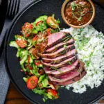 Overhead Thai Crying Tiger Steak with a spicy dipping sauce, rice, and tomato and cucumber salad.