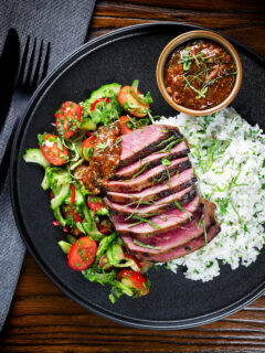 Overhead Thai Crying Tiger Steak with a spicy dipping sauce, rice, and tomato and cucumber salad.