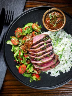 Overhead Thai Crying Tiger Steak with a spicy dipping sauce, rice, and tomato and cucumber salad.