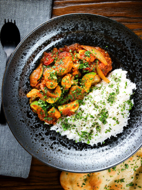 Overhead vegan vegetable rogan josh curry with rice, naan and fresh coriander.