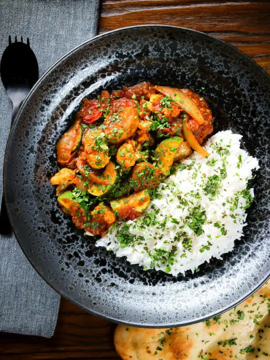 Overhead vegan vegetable rogan josh curry with rice, naan and fresh coriander.