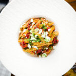 Overhead rose harissa, sun-dried tomato, pepper and feta cheese pasta.