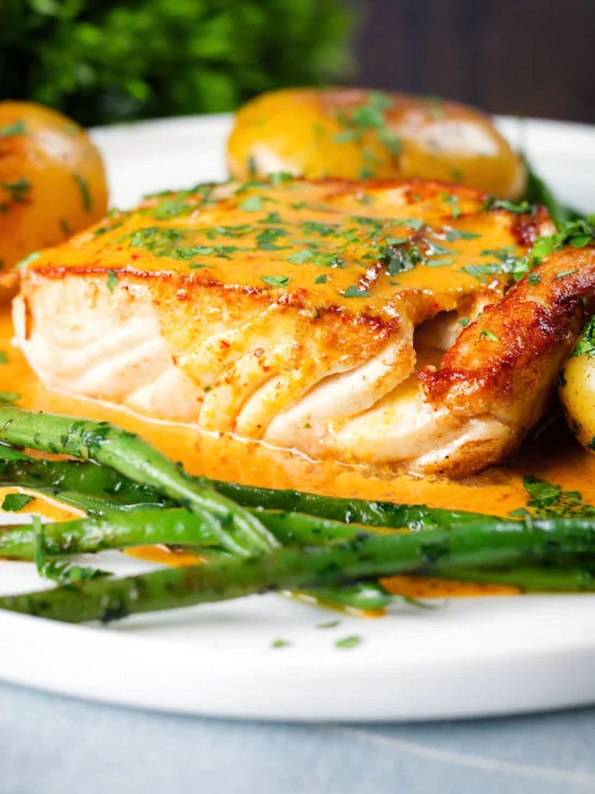 Close-up fried halibut with Thai yellow curry sauce, potatoes, green beans and coriander.