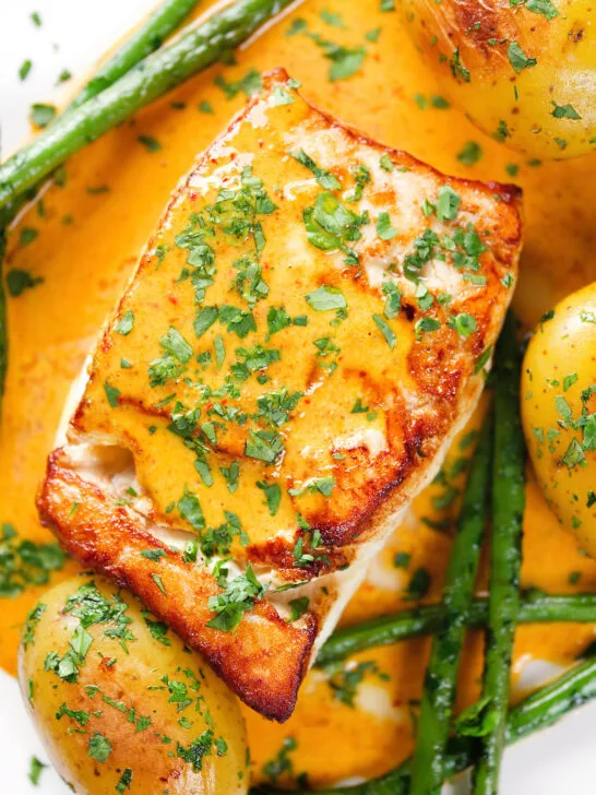 Close-up overhead fried halibut with Thai yellow curry sauce, potatoes, green beans and coriander.