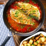 Overhead bourdeto, sea bass stew with paprika in a cooking pan with crispy potatoes.
