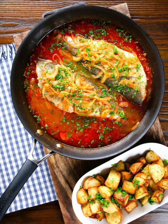 Overhead bourdeto, sea bass stew with paprika in a cooking pan with crispy potatoes.