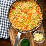 Overhead chicken and chorizo risotto with peas, Manchego cheese in a cooking pan.