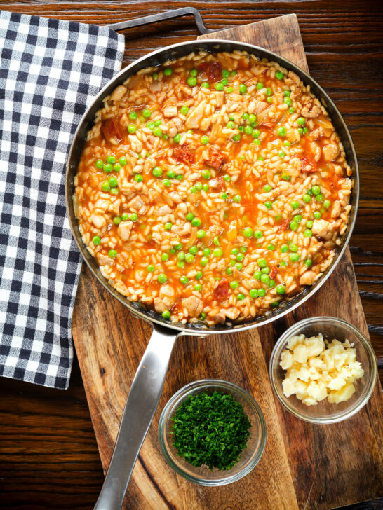 Overhead chicken and chorizo risotto with peas, Manchego cheese in a cooking pan.