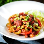 Spicy dragon chicken with peppers and cashew nuts, served with rice and spring onions.