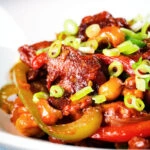 Close-up spicy dragon chicken with peppers and cashew nuts, served with rice and spring onions.