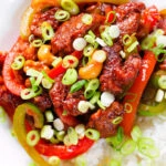 Close-up overhead spicy dragon chicken with peppers and cashew nuts, served with rice and spring onions.