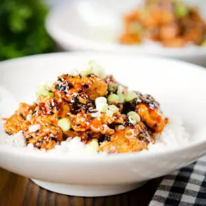 Crispy sesame chicken with a sweet sticky sauce served with white rice and spring onions.