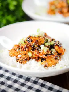 Crispy sticky sesame chicken served with white rice and spring onions.