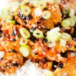 Close-up crispy sticky sesame chicken served with white rice and spring onions.
