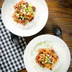 Overhead crispy sticky sesame chicken served with white rice and spring onions.
