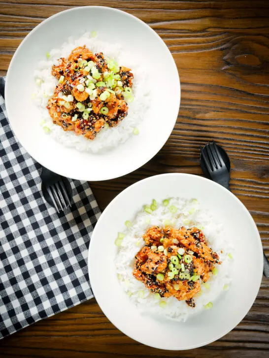 Overhead crispy sticky sesame chicken served with white rice and spring onions.