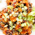 Close-up overhead crispy sticky sesame chicken served with white rice and spring onions.