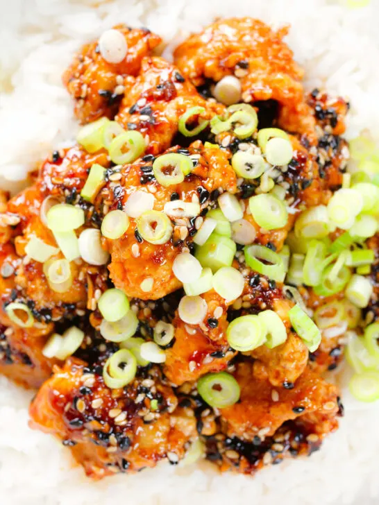 Close-up overhead crispy sticky sesame chicken served with white rice and spring onions.