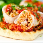 Close-up baked chorizo and brown rice stuffed squid in tomato sauce, served on focaccia.