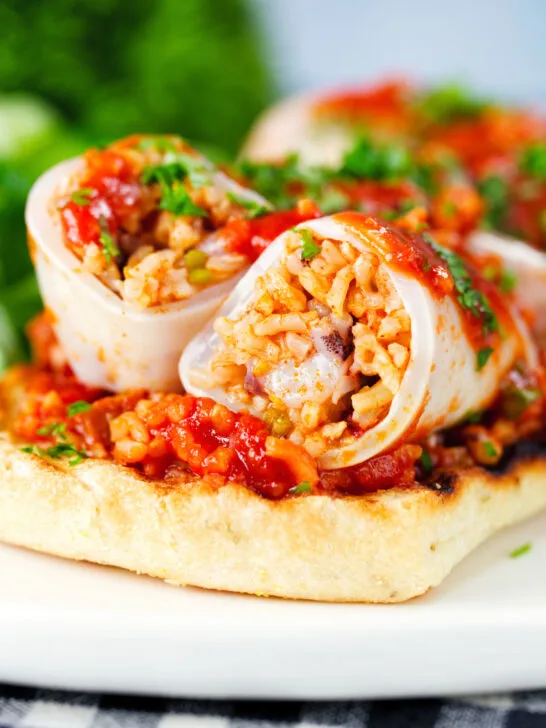 Close-up baked chorizo and brown rice stuffed squid in tomato sauce, served on focaccia.